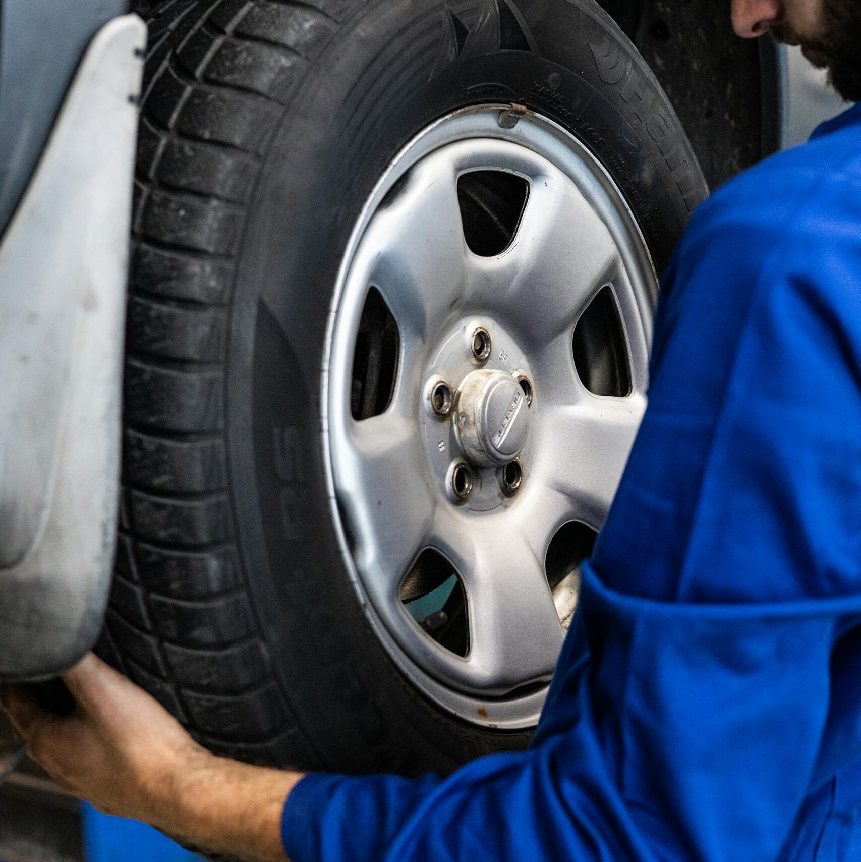 A mechanic in blue uniform closely examines a car wheel for repairs.